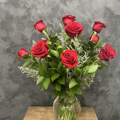 Vase on a table with one dozen red roses.