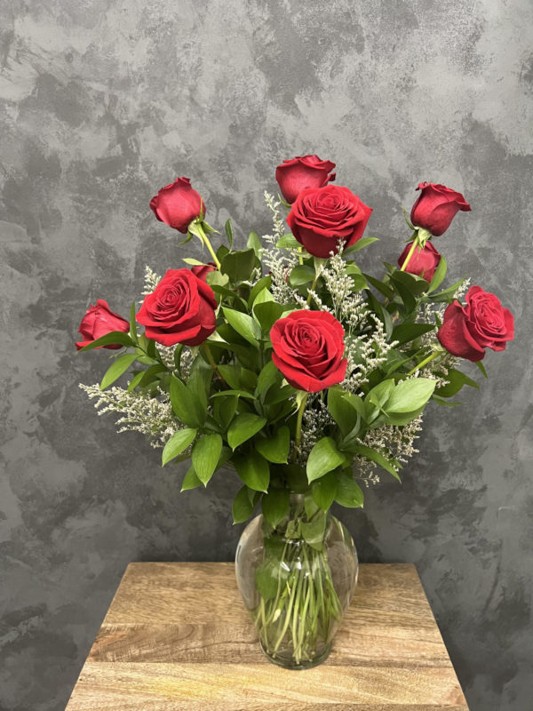 Flower arrangement of one dozen red roses and greenery in a glass vase.
