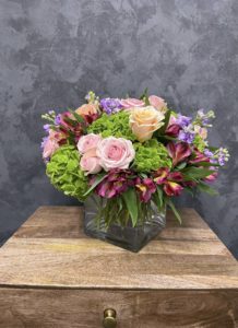 mothers day flower arrangement of roses, hydrangeas and lilacs are presented in a glass vase.