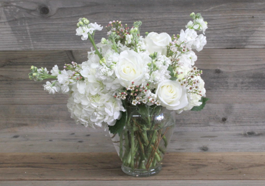 Tulips, carnations and seasonal foliage, all tied together and presented in a glass vase.