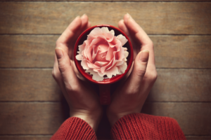 Woman holding hot cup of coffee with flower in the cup.