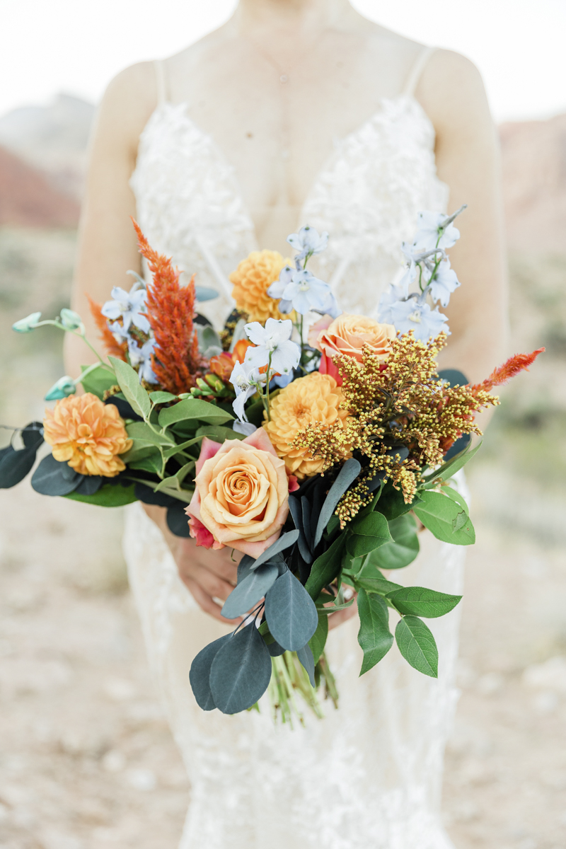 Woman holding peach, yellow and green wedding bouquet.