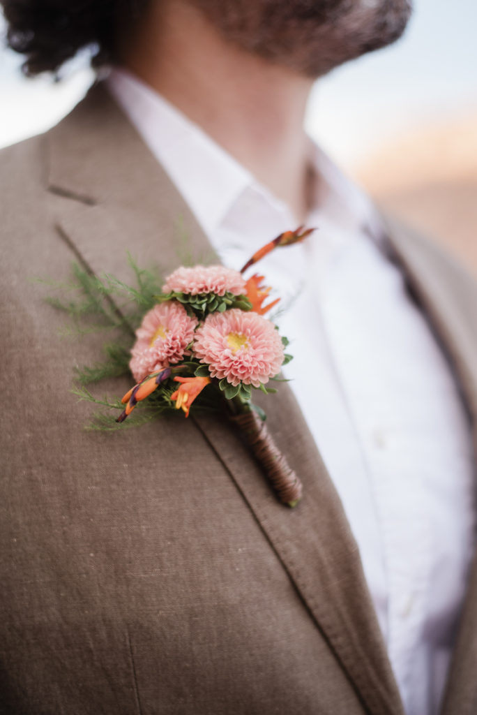 Groom with pink wedding boutonnière on a brown suit.