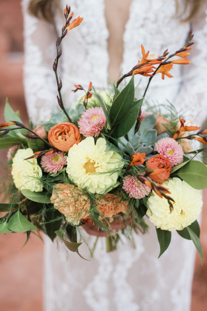 Bride holding a garden bouquet of yellow, pink and orange flowers.