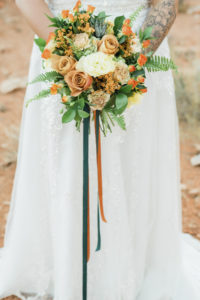 Wedding Florist Las Vegas Bride holding round wedding bouquet of orange flowers and greenery.