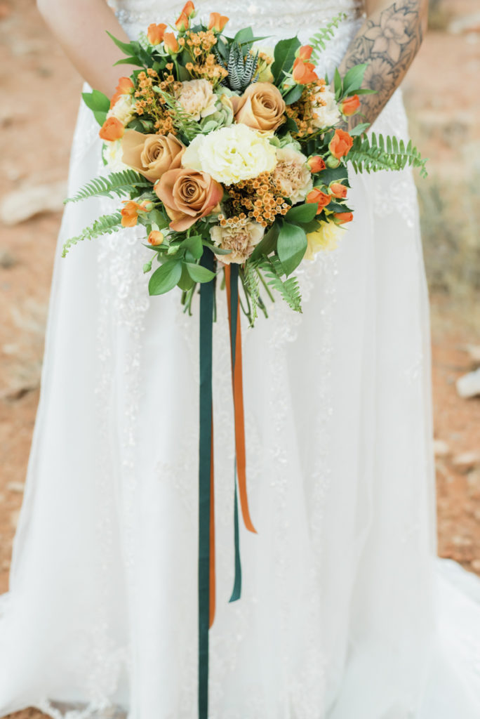 Bride holding round wedding bouquet of orange flowers and greenery.