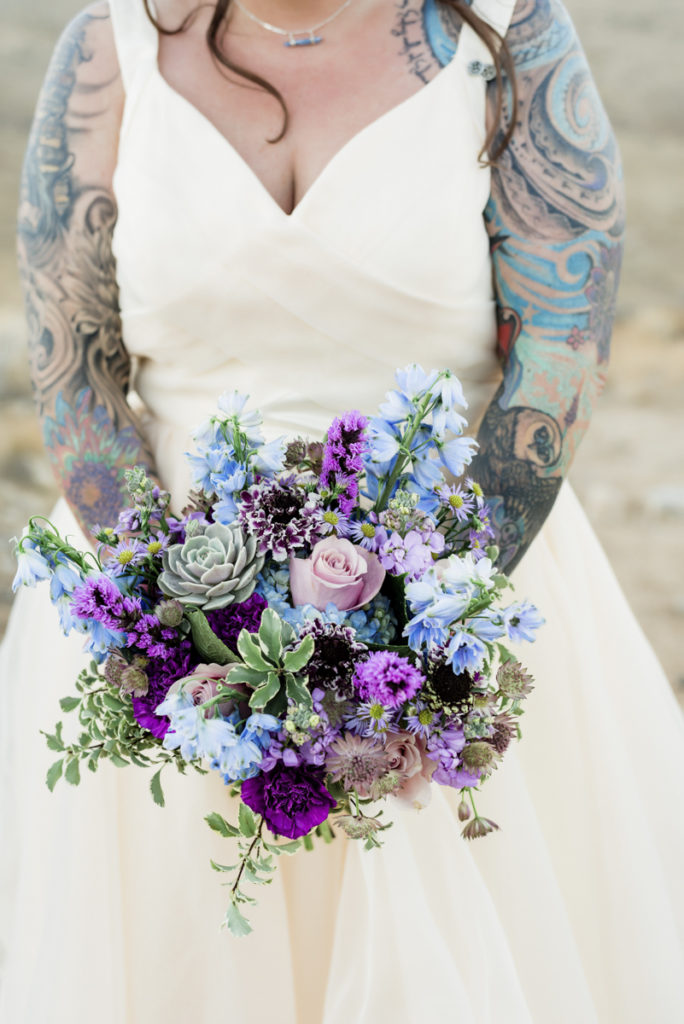 Bride holding wedding bouquet of purple flowers and greenery.