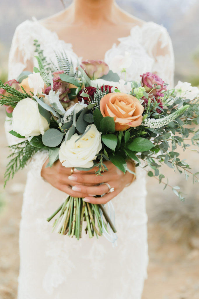 Bride holding wedding bouquet of mixed florals and greenery.