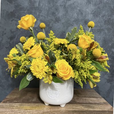 Yellow themed flower arrangement in a white vase with a sun design.