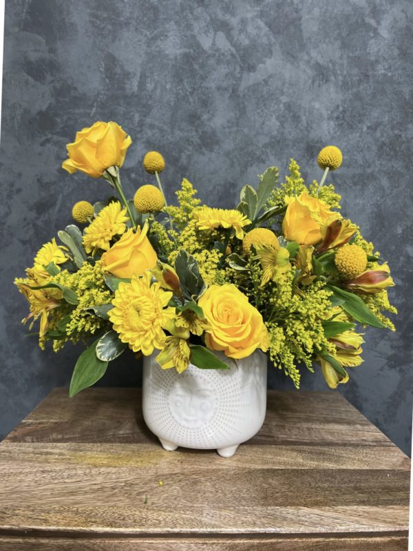 Yellow themed flower arrangement in a white vase with a sun design.