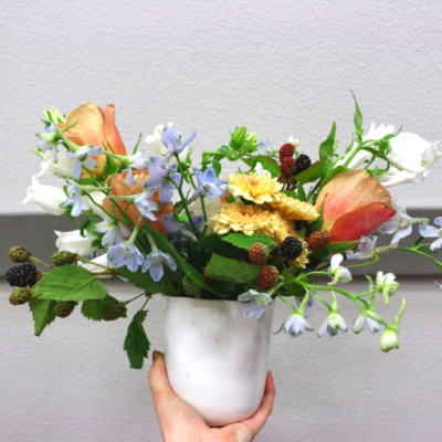 Small flower bouquet in a white vase being hand delivered.