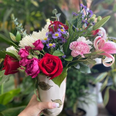 Bouquet of flowers in a white vase being hand delivered.