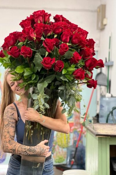 Person delivering a glass vase of 100 red roses.