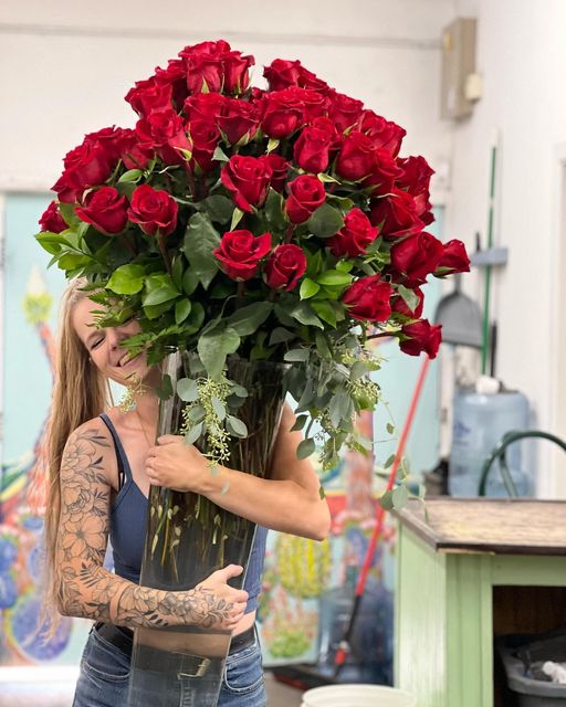 Person delivering a glass vase of 100 red roses.