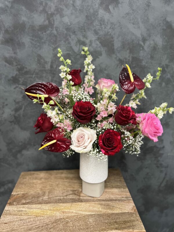 Valentine's flower arrangement of red and pink roses and red anthurium in a white ceramic vase.