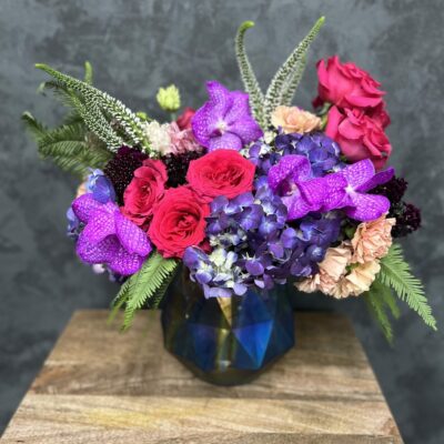Valentine's flower arrangement of pinks and purples in a blue, glass vase.