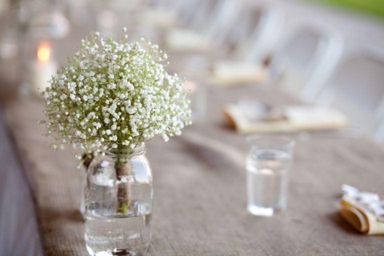 Mason jar on a table filled with white flowers.