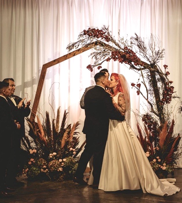 Bride and groom kissing at the altar decorated with flowers and feathers.