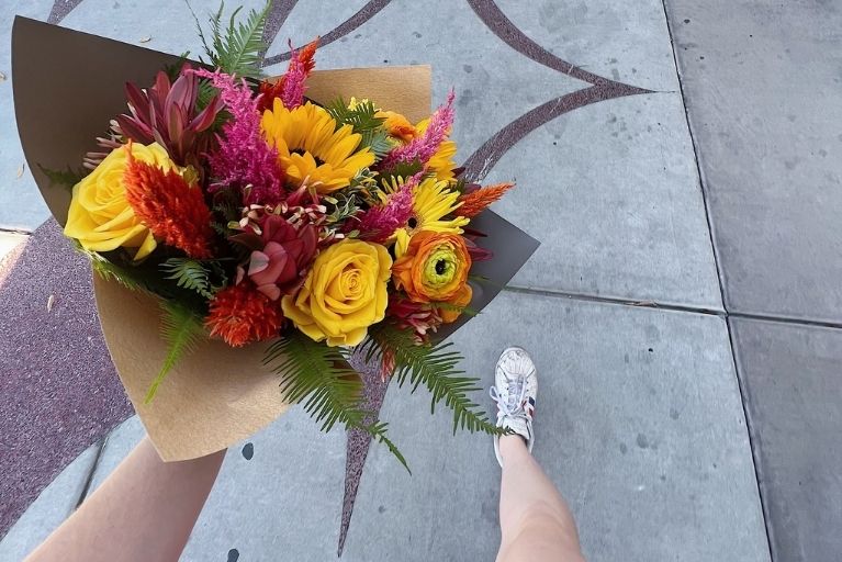 over head view of a person holding a bouquet of colorful flowers in brown paper wrap as she walks on a sidewalk