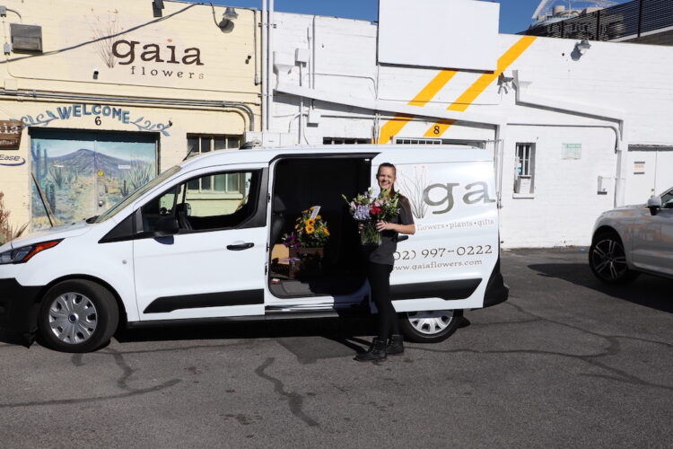 person standing next to a flower delivery van holding a flower arrangement