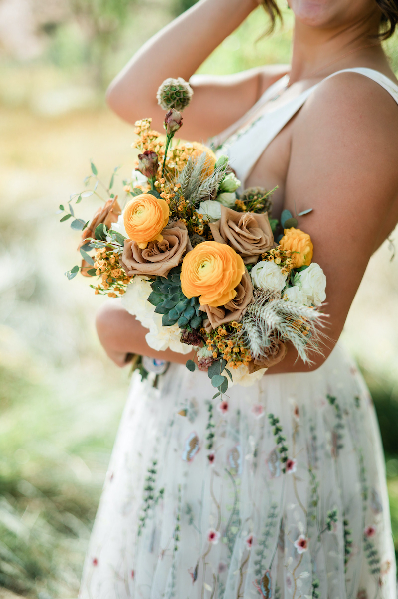 wedding-florist-5 bride holding a wedding bouquet with peach and white flowers, succulents, and feathers