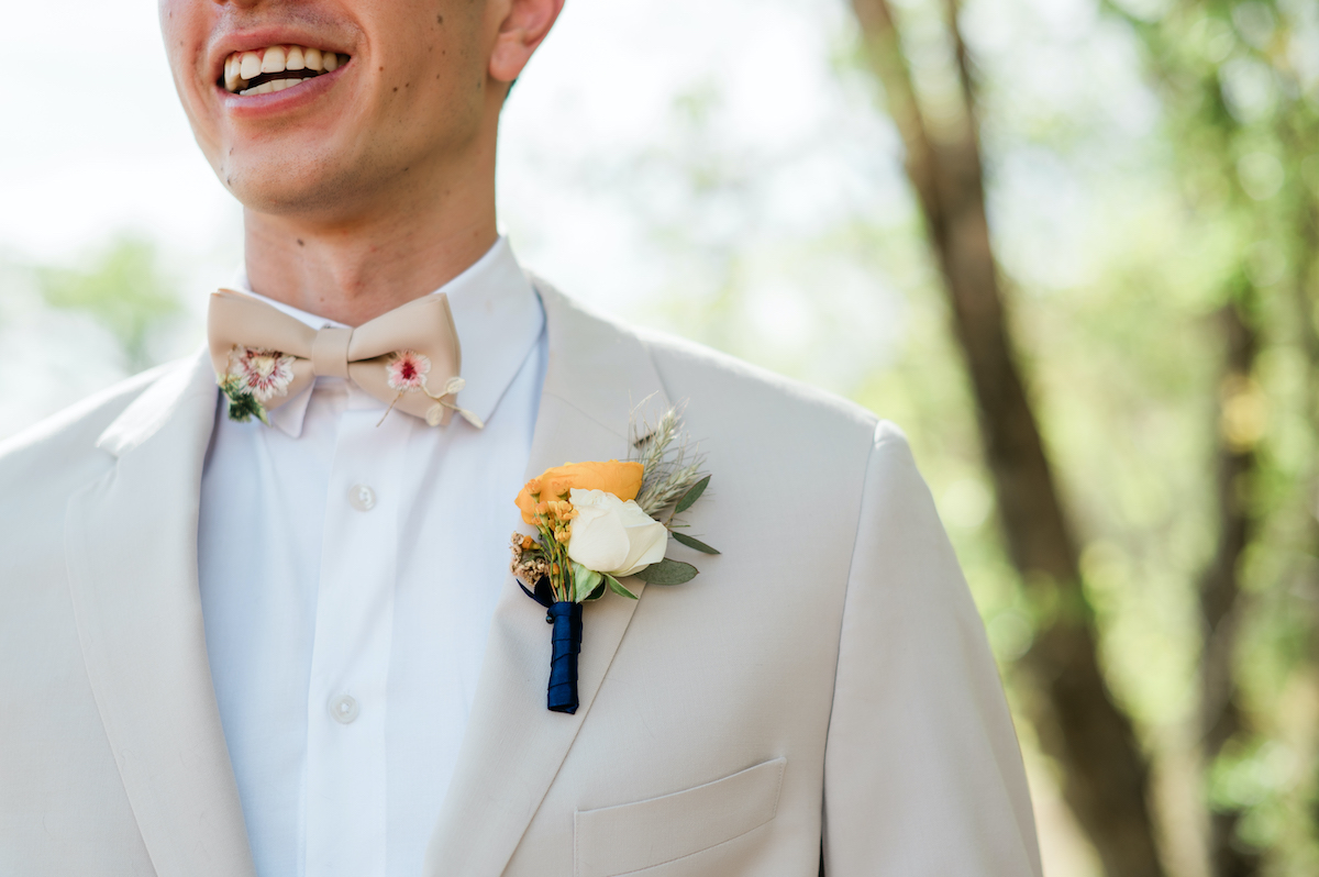 groom in a white suite with a yellow and white boutonnière