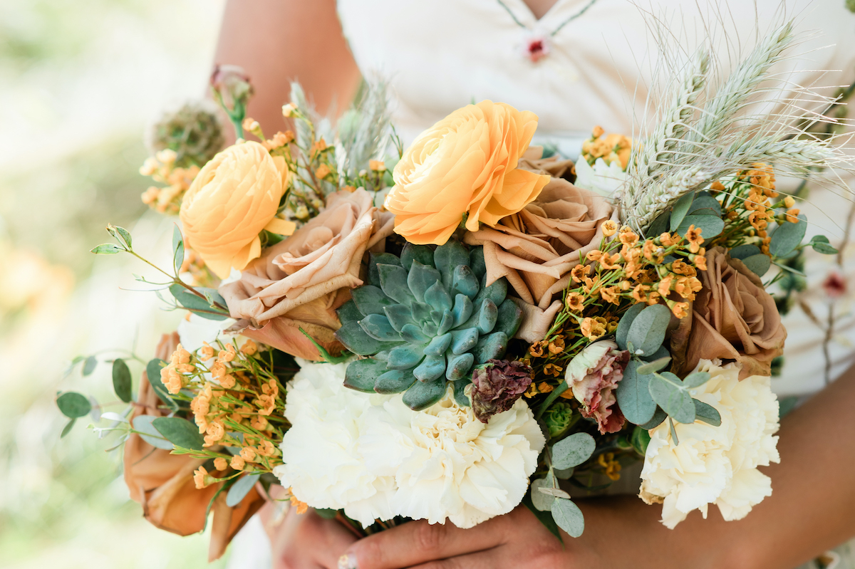 wedding bouquest of peach and white flowers with succulents and feathers