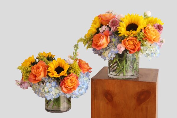 two flower arrangements of hydrangea, sunflowers, roses and in a round glass vase