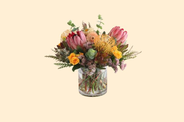 flower arrangement of proteas and yellow flowers in a glass vase