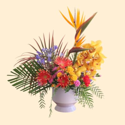 large flower arrangement with bird of paradise, orchids, greenery, and other small flowers in a purple vase