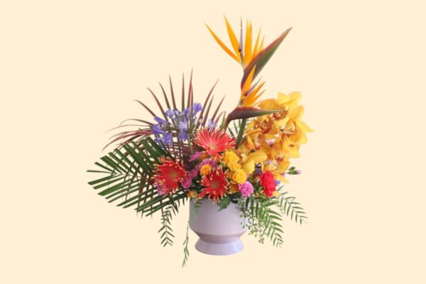 large flower arrangement with bird of paradise, orchids, greenery, and other small flowers in a purple vase